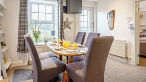 A dining area with a table set for four, chairs, a star decoration on the wall, a flat-screen TV mounted above the table, and a window with curtains. - 3 bedroom accommodation in New Quay (New Quay)