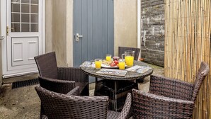 A patio with wicker furniture, a table with a newspaper, and a fruit plate with drinks. - 3 bedroom accommodation in New Quay (New Quay)