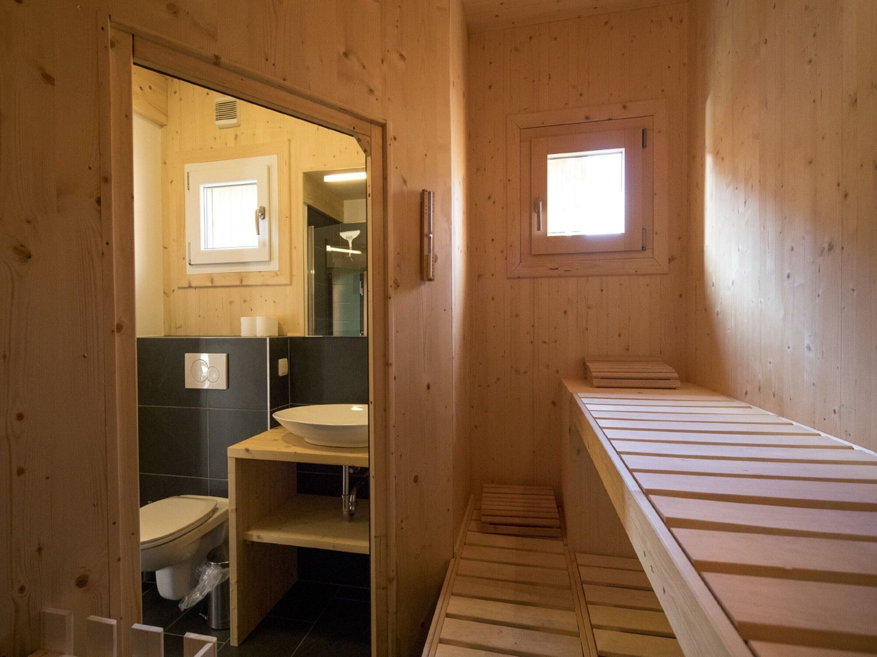 A wooden cabin-style bathroom with a toilet, sink, and a bench.