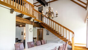 Une salle à manger spacieuse avec une longue table et de nombreuses chaises, un escalier en bois et un lustre.