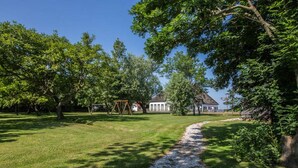 Un parc verdoyant avec un sentier de gravier menant à un bâtiment blanc surmonté d’un toit rouge.