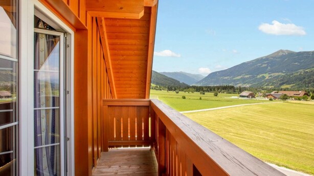 A wooden balcony with a view of a green field and mountains. - Modern Apartment Right Next to the ski Lift (Sankt Margarethen im Lungau)