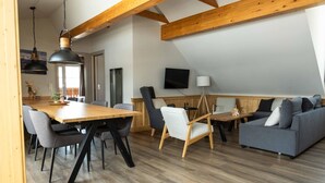 A modern living room with a wooden dining table, grey sofas, and a TV mounted on the wall. - Modern Apartment Right Next to the ski Lift (Sankt Margarethen im Lungau)