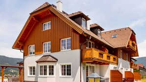 A large, two-story wooden house with a balcony, a covered porch, and a well-maintained lawn. - Modern Apartment Right Next to the ski Lift (Sankt Margarethen im Lungau)