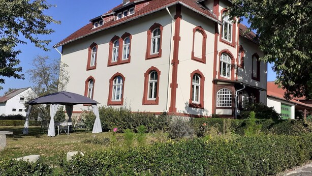 A large, historic building with a red-tiled roof and multiple arched windows. - Ferienwohnung mit Garten auf dem Bauernhof (Trendelburg)