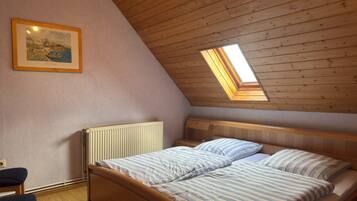 A bedroom with a sloped ceiling, a bed with striped bedding, a radiator, a framed picture on the wall, and a skylight.