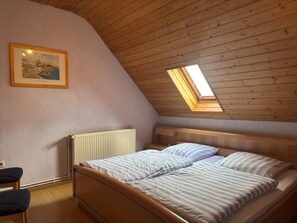 A bedroom with a sloped ceiling, a bed with striped bedding, a radiator, a framed picture on the wall, and a skylight. - Ferienwohnung mit Garten auf dem Bauernhof (Trendelburg)