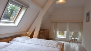 A bedroom with a sloped ceiling, a skylight, a bed, a chair, and a window with curtains. - Apartment Bergen aan Zee Near Beach (Bergen aan Zee)