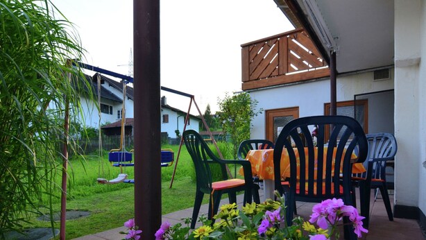 A patio area with a table and chairs, surrounded by flowering plants and a swing set. - Gemutliche Ferienwohnung, Lechbruck (Lechbruck)