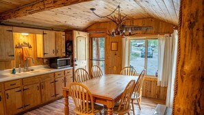 Interno di una baita di legno con tavolo da pranzo, sedie, una cucina con forno a microonde e un lampadario.