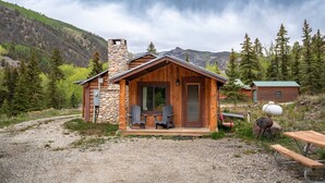Una baita rustica con un camino in pietra, rivestimento in legno e un portico con due poltrone Adirondack.