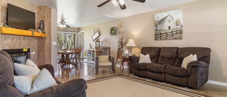 A spacious living room with a large brown sofa, a dark brown armchair, and a television mounted on the wall.