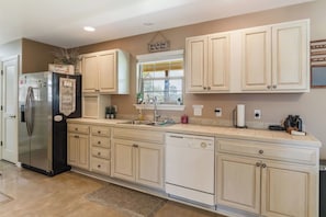 A kitchen with a stainless steel refrigerator, white cabinetry, a dishwasher, and a window with a view.