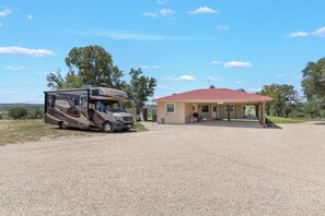 A recreational vehicle parked in front of a building with a red roof, a covered outdoor seating area, and a gravel ground.