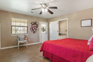 A bedroom with a bed, a chair, a ceiling fan, a door, and a window with blinds.