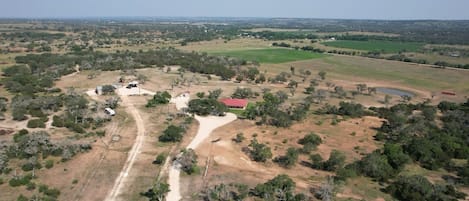 An aerial view of a rural property with multiple buildings, a dirt road, and surrounding vegetation.