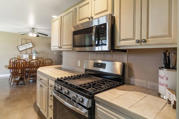 A kitchen with a gas stove, oven, microwave, and cabinets. There is a dining table with chairs and a ceiling fan.