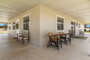 A covered patio area with a concrete floor, wooden benches, metal chairs, and a table.