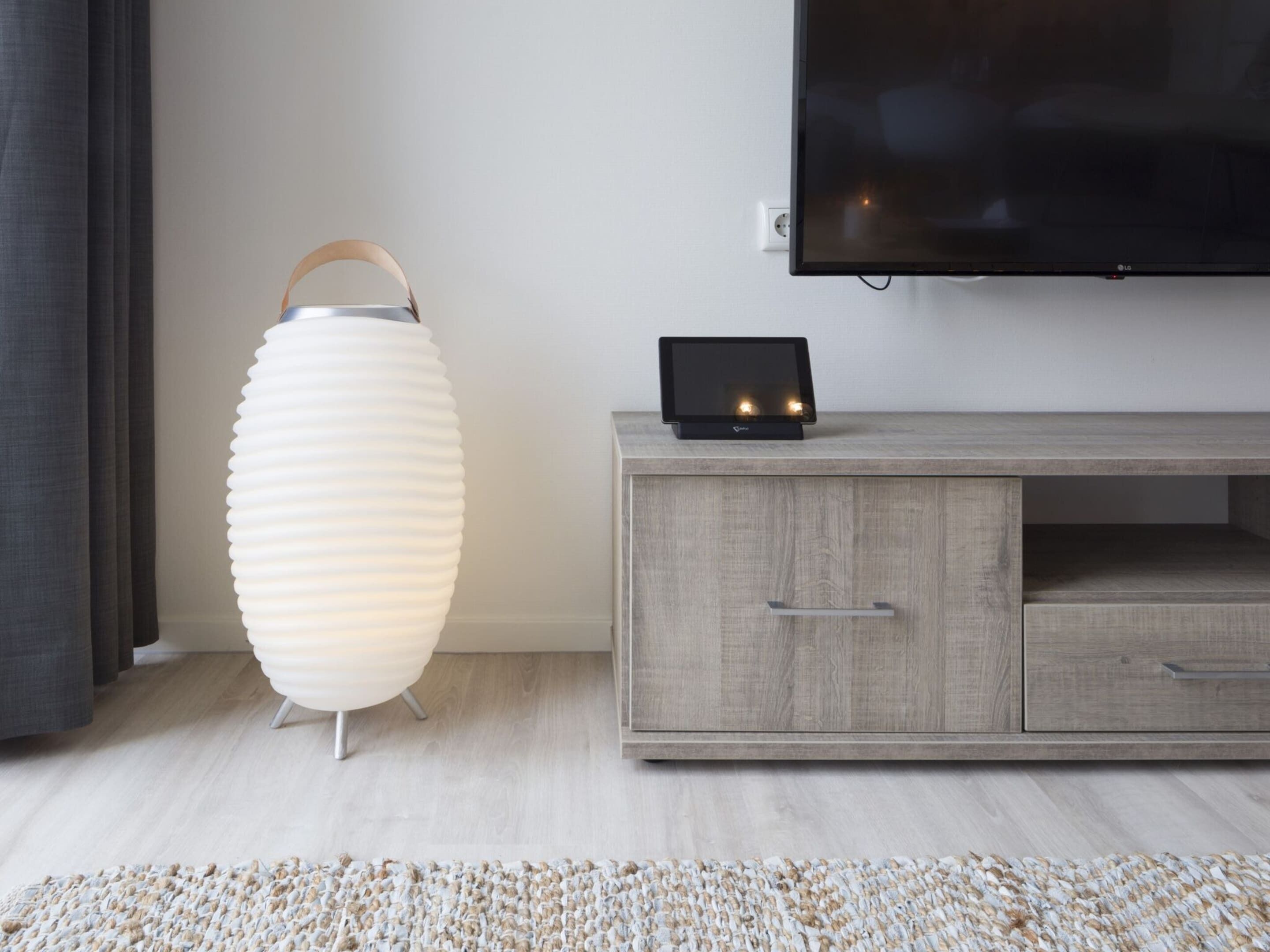 A modern living room with a white lamp, a flat-screen TV, and a wooden cabinet.