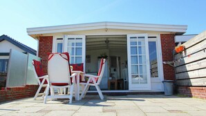 Un bâtiment d’un seul étage avec une porte de garage, une terrasse avec des chaises blanches et une table, et un ciel bleu dégagé.