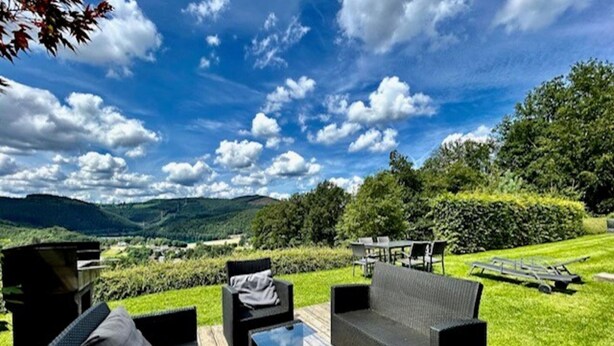 Un espace extérieur aménagé avec des meubles en osier et une table en verre, offrant une vue sur un paysage verdoyant et des collines.