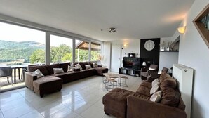 Un salon spacieux avec un grand canapé d’angle, un coin repas comprenant une table et des chaises, et une vue sur l’extérieur.