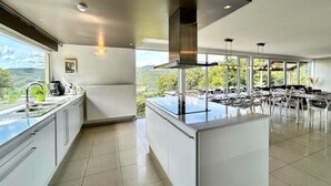 Une cuisine moderne dotée d’un îlot central, de grandes fenêtres et d’un coin repas avec des sièges extérieurs.