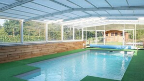Une piscine intérieure dotée d’un toit en verre, de murs en bois et offrant une vue sur l’extérieur.