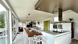 Une cuisine moderne dotée d’un grand îlot central, de meubles blancs et d’un coin repas avec des chaises blanches.