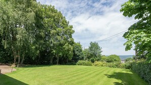 A well-maintained lawn with a variety of trees and shrubs, a clear sky, and a distant view of a building. - Rustic Cottage in Jevigne (Lierneux)