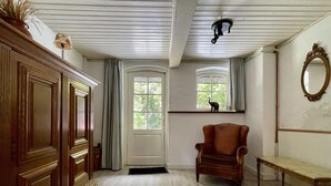 A room with a wooden wardrobe, a brown armchair, a bench, a door with a window, and a ceiling light fixture. - Farmhouse in Sint Joost With Pool & BBQ (Sint Joost)