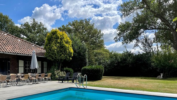 A swimming pool with a tiled deck, outdoor seating, and a building with a tiled roof. - Farmhouse in Sint Joost With Pool & BBQ (Sint Joost)