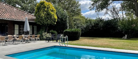 A swimming pool with a tiled deck, outdoor seating, and a building with a tiled roof.
