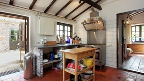 A kitchen with a brick wall, a wooden table, and a stainless steel stove. - Farmhouse in Sint Joost With Pool & BBQ (Sint Joost)