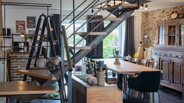 A modern kitchen with a brick wall, a staircase with metal railings, and wooden furniture. - Tranquil Stay in Ardennes (Doische)