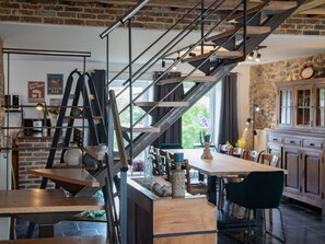 A modern kitchen with a brick wall, a staircase with metal railings, and wooden furniture.