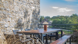A stone wall, a wooden table with benches, and a view of greenery and buildings in the distance. - Tranquil Stay in Ardennes (Doische)
