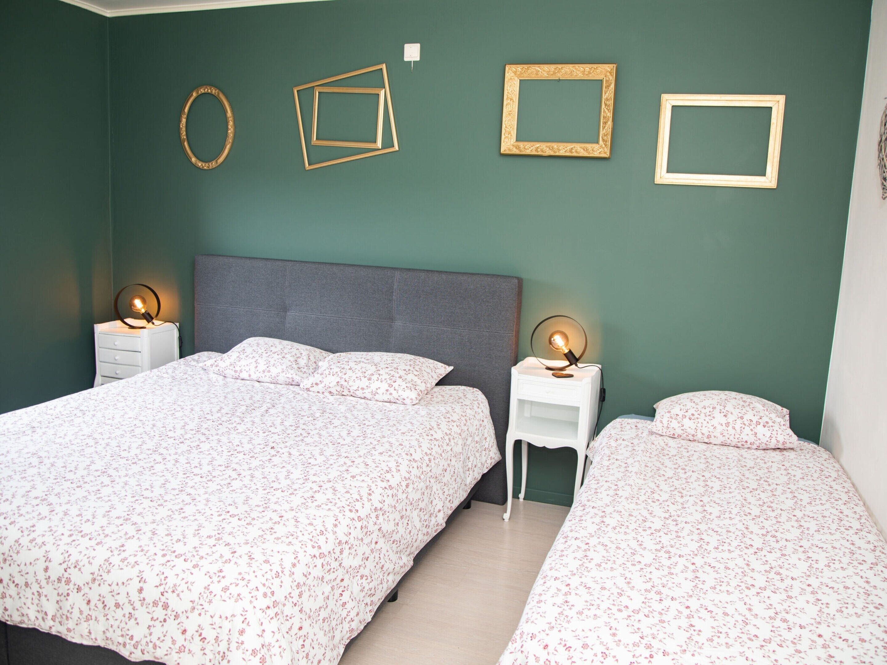 A bedroom with two beds, a grey headboard, and wall-mounted picture frames.