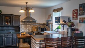 A kitchen with dark wooden cabinets, a brick accent wall, a central island with chairs, a hanging light fixture, and a microwave. - Tranquil Stay in Ardennes (Doische)