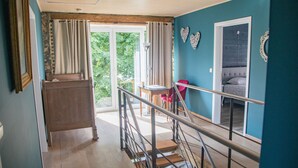 A staircase leading to a balcony with a view of greenery, a dining area with a table and chairs, and a bed with a headboard. - Tranquil Stay in Ardennes (Doische)