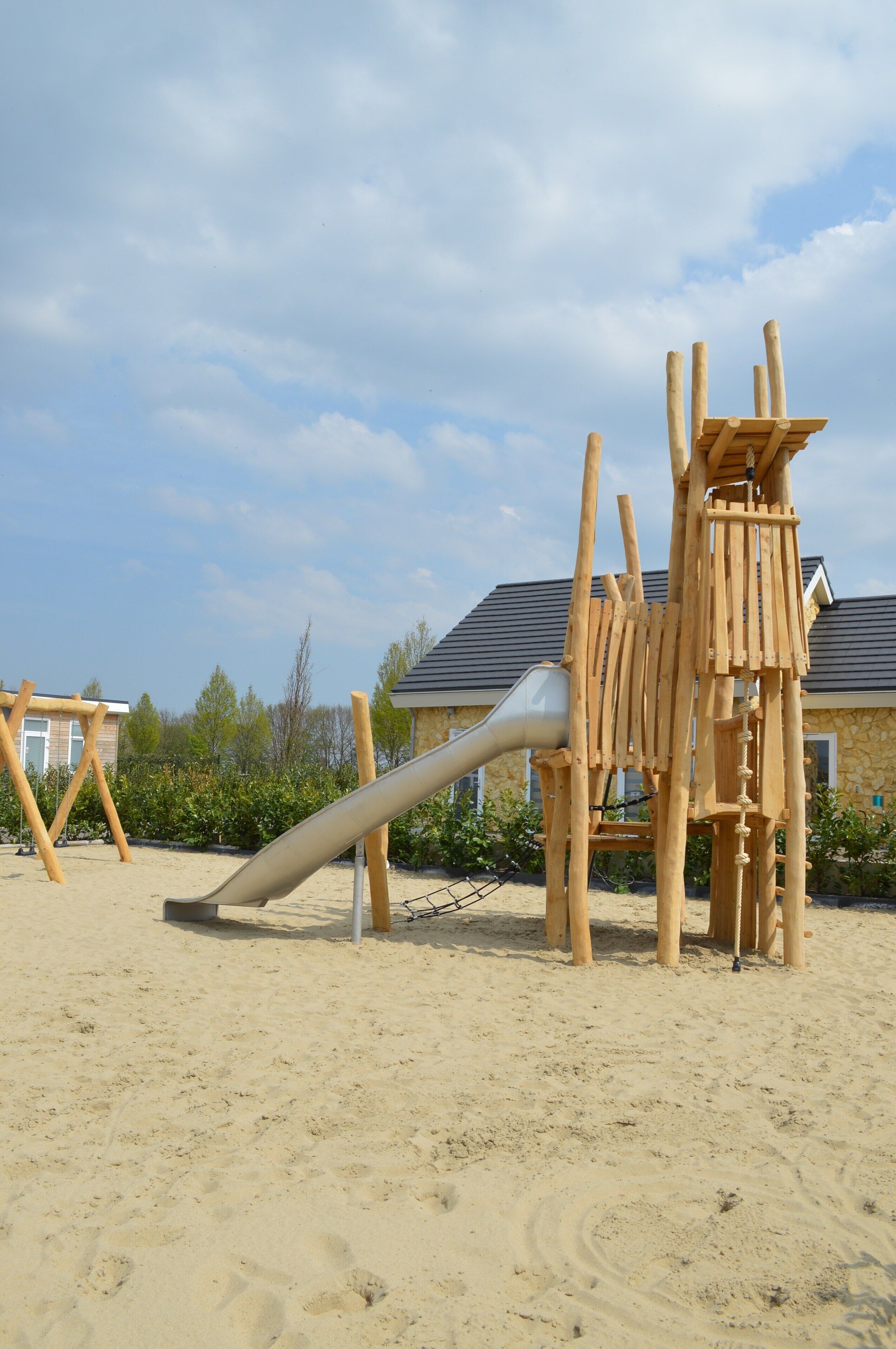 Une aire de jeux avec un toboggan et des structures d’escalade sur un sol sablonneux.