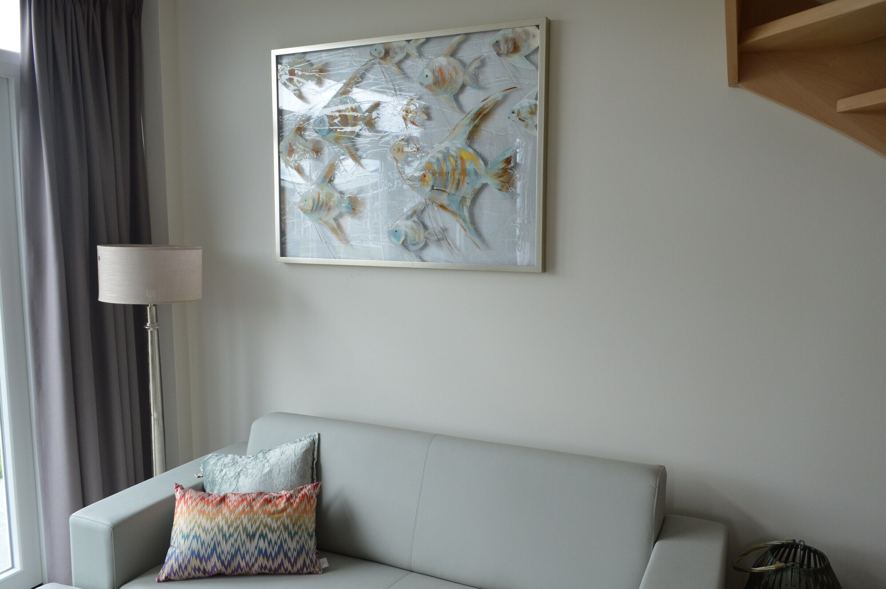 A modern living room with a grey sofa, a colorful pillow, a floor lamp, and a wall-mounted artwork of fish.