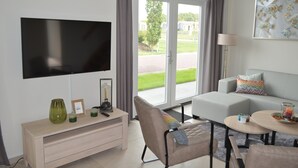 Una sala de estar moderna con un televisor de pantalla plana, un sofá, una mesa de centro y vistas al exterior a través de amplios ventanales.