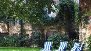 Un patio con tres sillones a rayas, un edificio de piedra cubierto de hiedra y un césped.