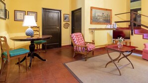 Una sala de estar con una mesa de madera, una silla, un sofá, una escalera y un cuadro en la pared.