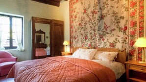 Un dormitorio con una cama grande, un armario de madera, un espejo y un papel tapiz con motivos florales.
