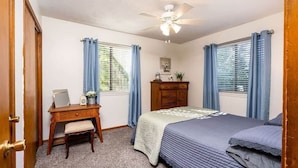 Une chambre à coucher comprenant un lit, un bureau, une chaise, une commode et un ventilateur de plafond.