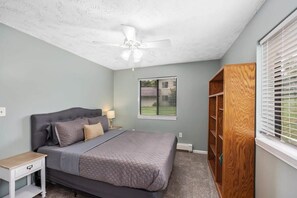 A bedroom with a bed, nightstand, ceiling fan, window with blinds, and a wooden wardrobe. - Charming 2-unit retreat in Rockford (Rockford)
