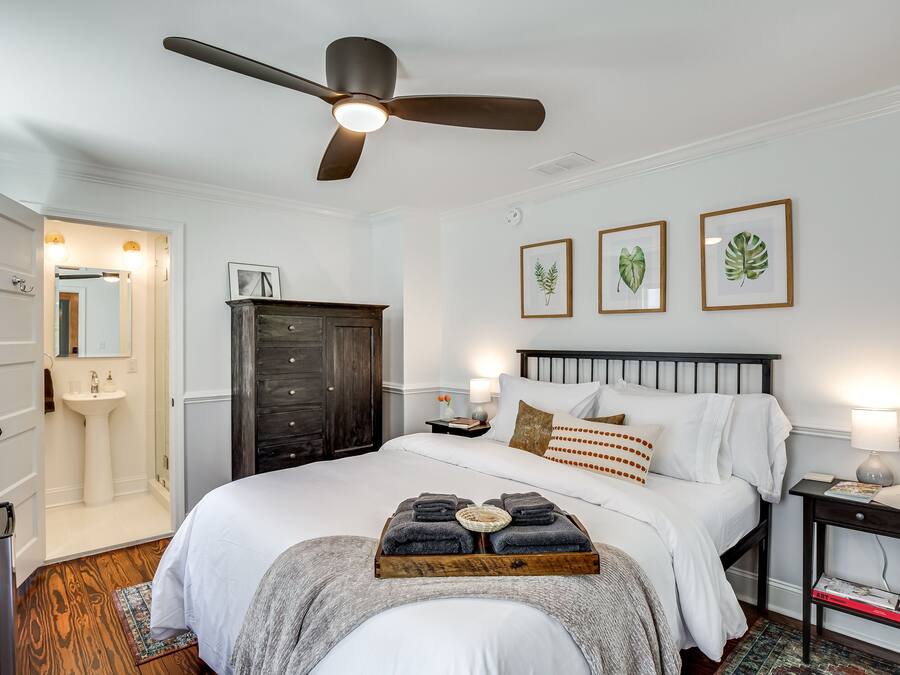 Un dormitorio ordenado con cama, mesita de noche y ventilador de techo.