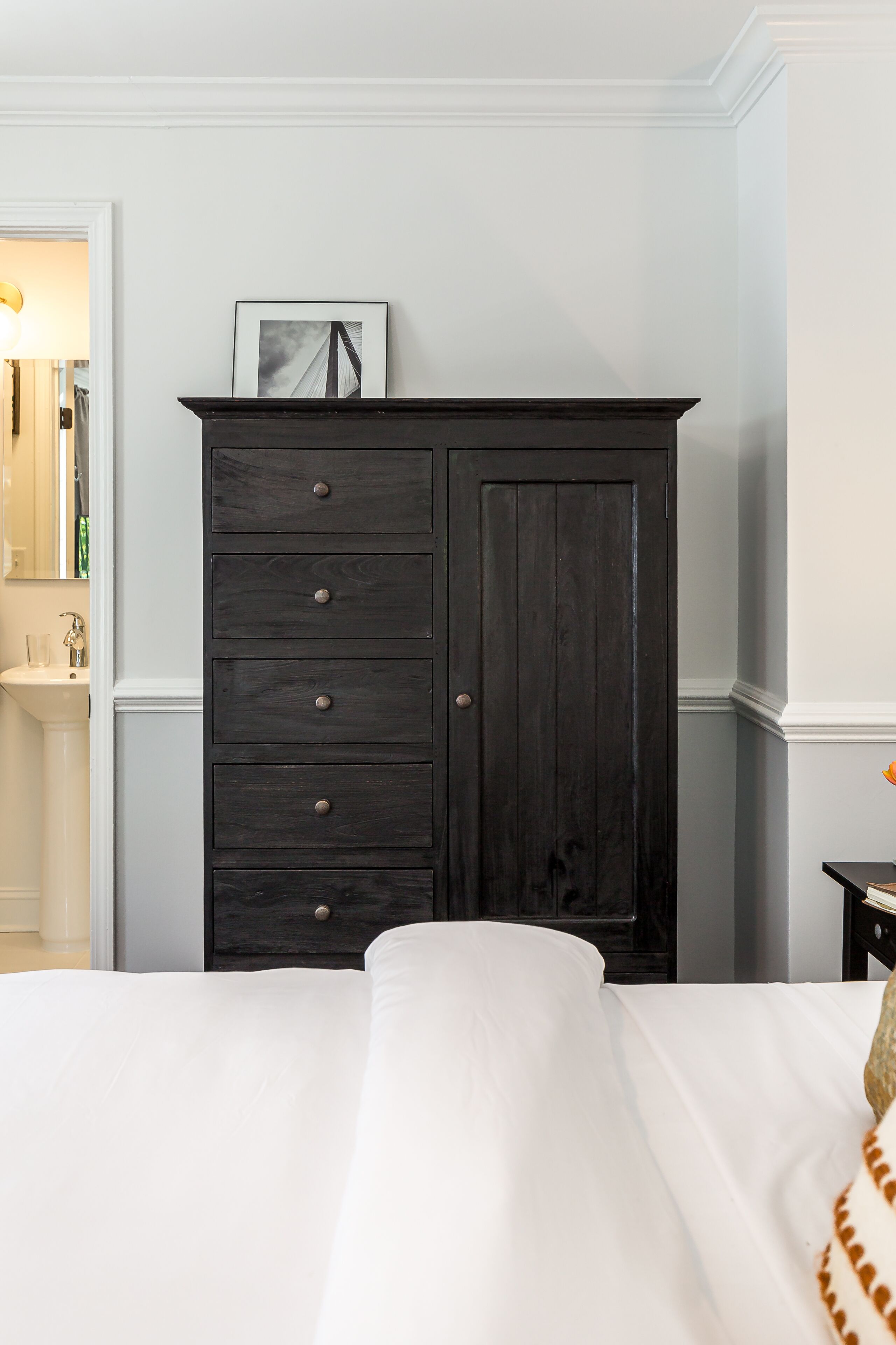 A bedroom with a dark wooden dresser, a white bed, and a small bedside table.